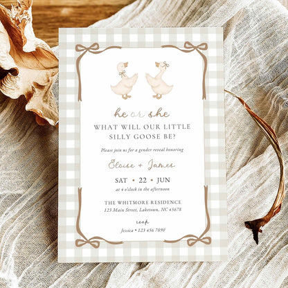 A baby shower invitation card featuring a gingham border and duck illustrations, styled on a textured fabric background with dried leaves and antlers.