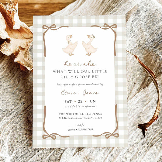 A baby shower invitation card featuring a gingham border and duck illustrations, styled on a textured fabric background with dried leaves and antlers.