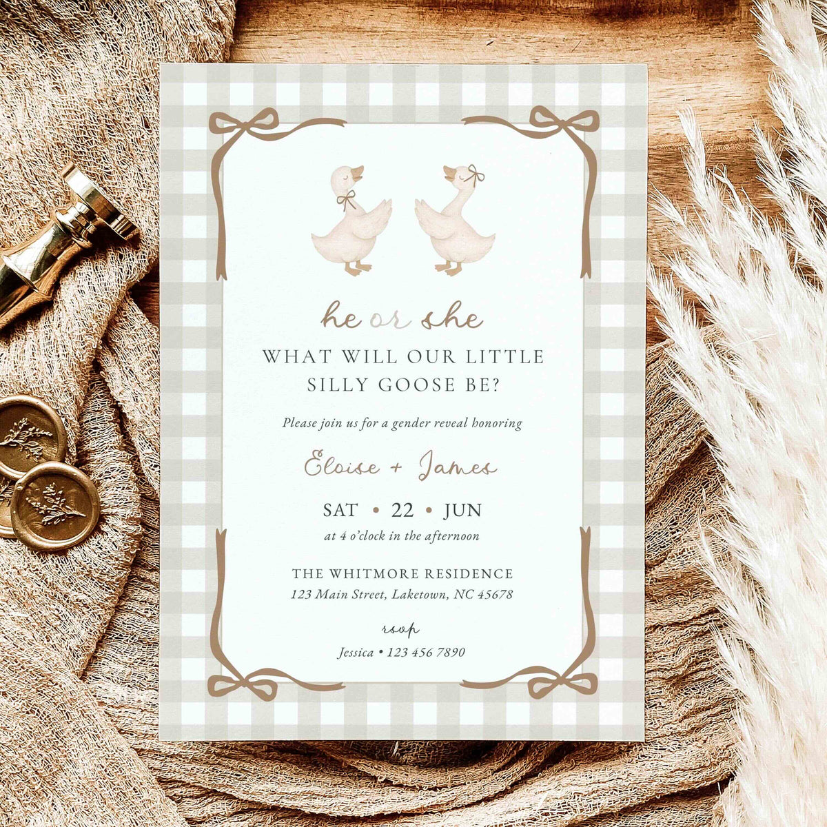 A baby gender reveal invitation card styled on a rustic wooden surface with burlap, brass keys, and dried grass. The card features a white and beige gingham border, two watercolor geese, and brown text.