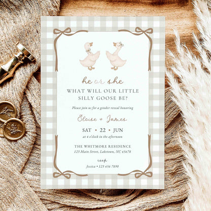A baby gender reveal invitation card styled on a rustic wooden surface with burlap, brass keys, and dried grass. The card features a white and beige gingham border, two watercolor geese, and brown text.