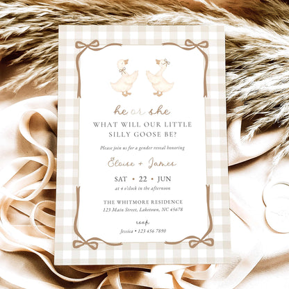A baby shower invitation card featuring a gingham border and two geese illustrations, styled on a beige fabric background with ribbon and faux fur.