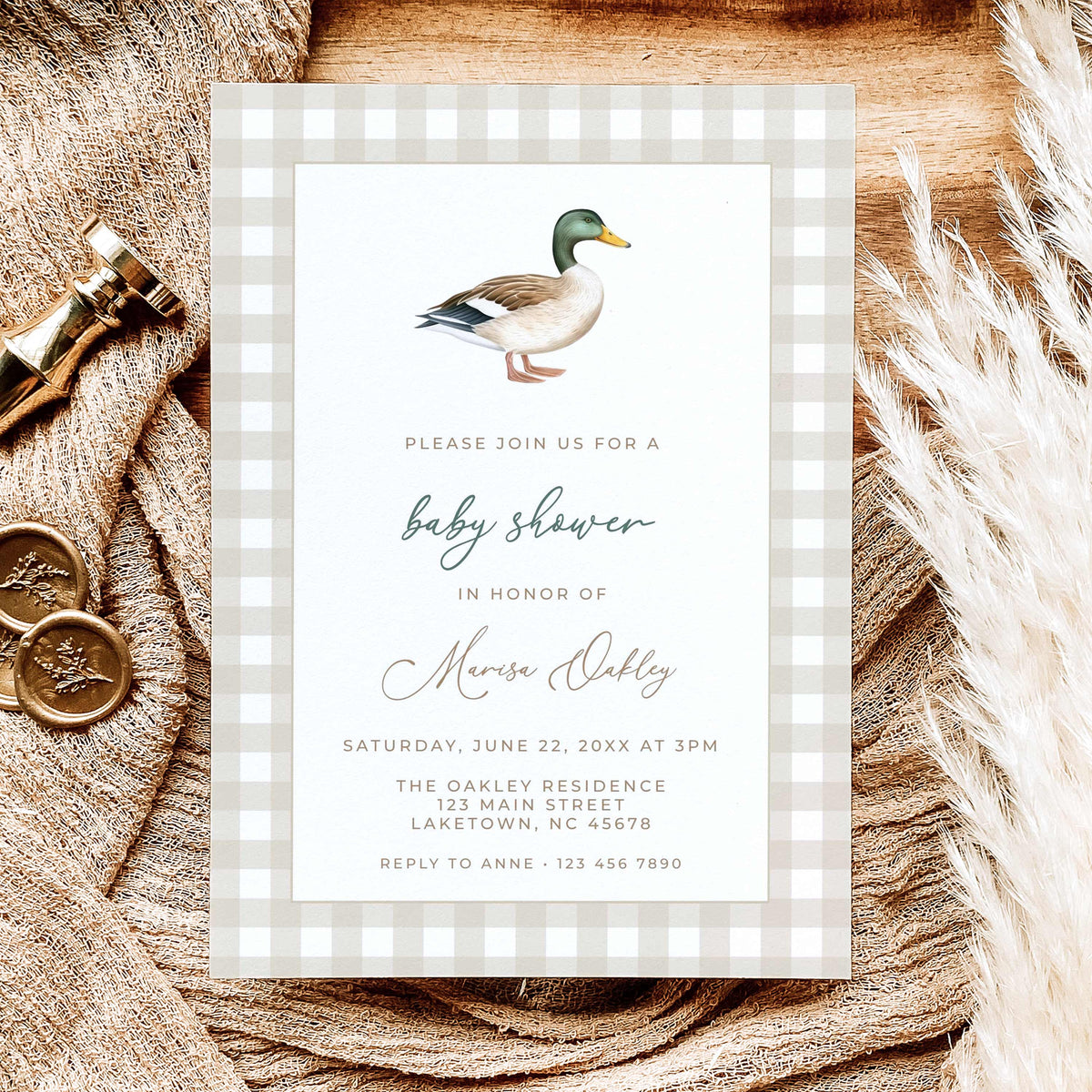 Mallard duck baby shower invitation featuring a watercolor mallard illustration, beige gingham border, and sage green script, displayed on natural linen with dried leaves.