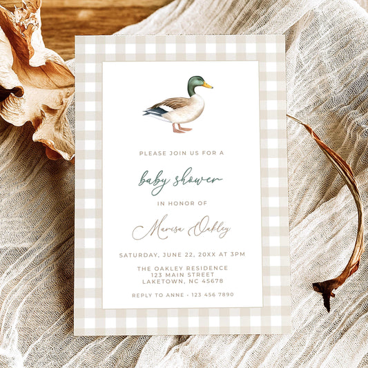 Mallard duck baby shower invitation featuring a watercolor mallard illustration, beige gingham border, and sage green script, displayed on natural linen with dried leaves.
