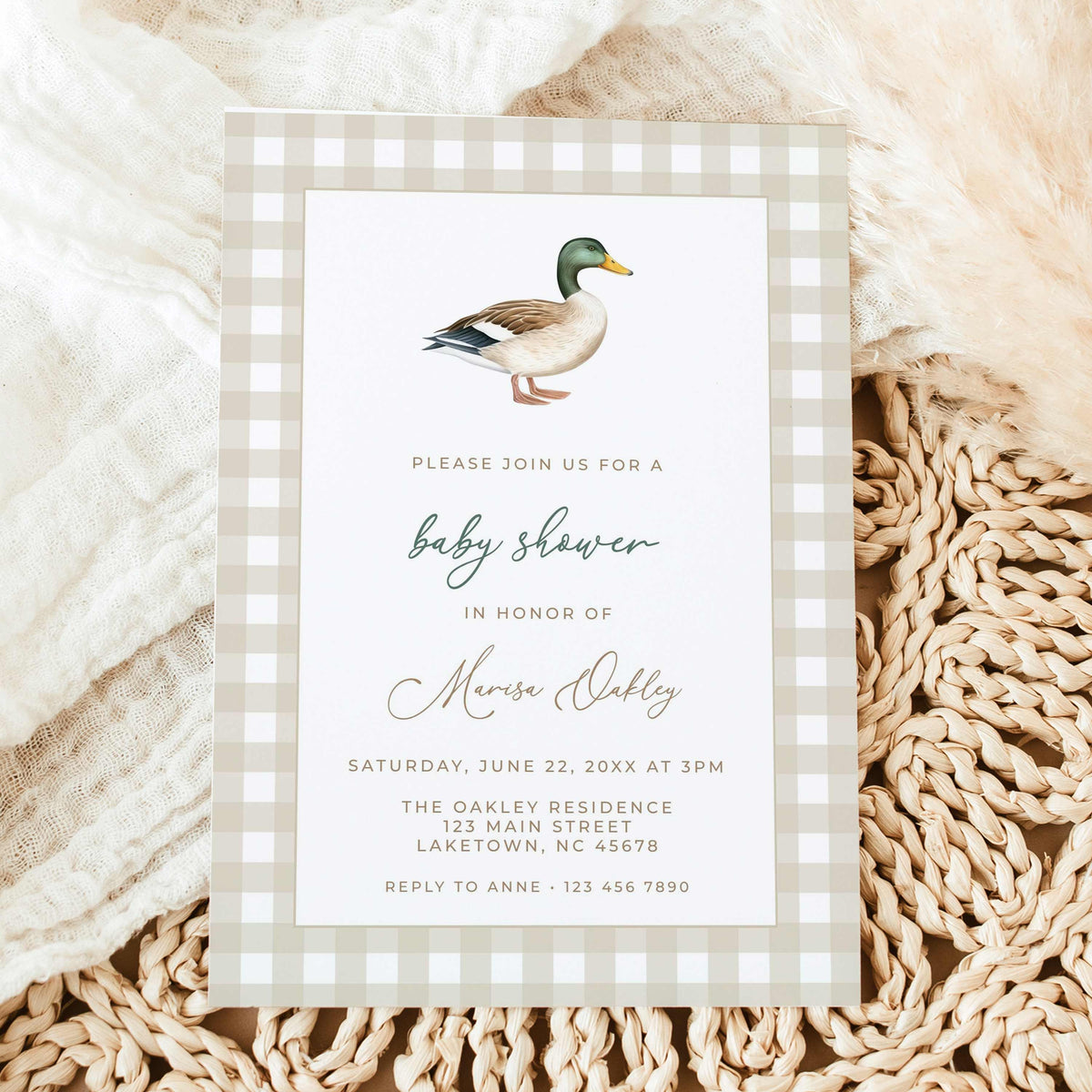 Mallard duck baby shower invitation featuring a watercolor mallard illustration, beige gingham border, and sage green script, displayed on natural linen with dried leaves.