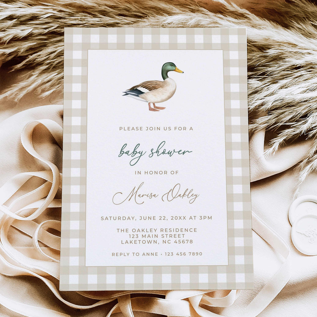 Mallard duck baby shower invitation featuring a watercolor mallard illustration, beige gingham border, and sage green script, displayed on natural linen with dried leaves.