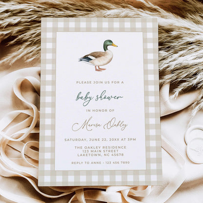Mallard duck baby shower invitation featuring a watercolor mallard illustration, beige gingham border, and sage green script, displayed on natural linen with dried leaves.