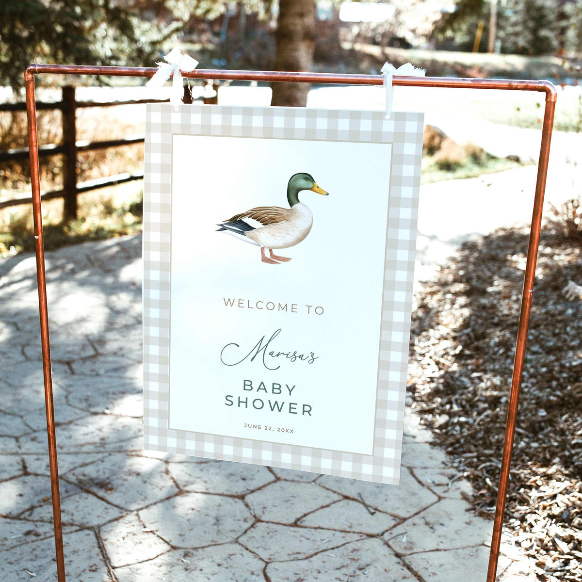 Mallard duck baby shower welcome sign featuring a watercolor mallard illustration, beige gingham border, and sage green lettering, displayed on a wooden easel outdoors.