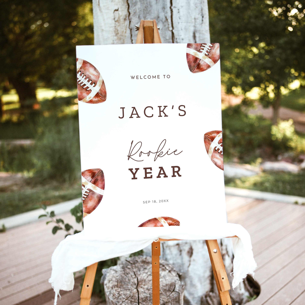 Rookie of the Year football first birthday welcome sign featuring vintage watercolor brown footballs, personalized birthday lettering, and a white background, displayed outdoors on a wooden easel.