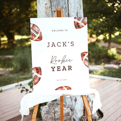 Rookie of the Year football first birthday welcome sign featuring vintage watercolor brown footballs, personalized birthday lettering, and a white background, displayed outdoors on a wooden easel.
