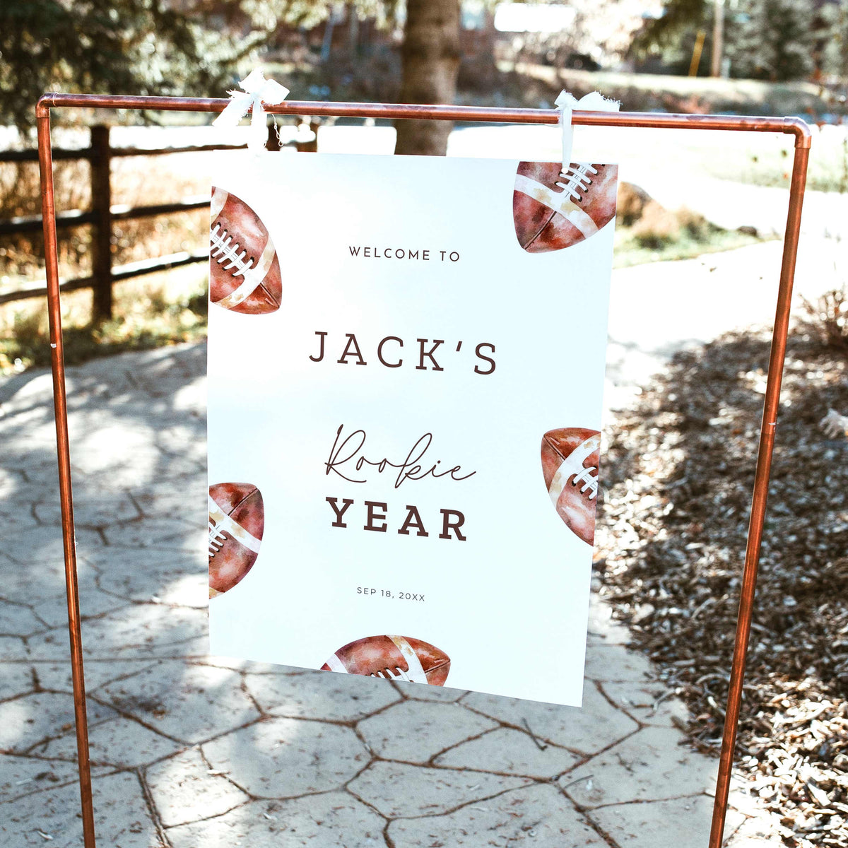 Rookie of the Year football first birthday welcome sign featuring vintage watercolor brown footballs, personalized birthday lettering, and a white background, displayed outdoors on a wooden easel.