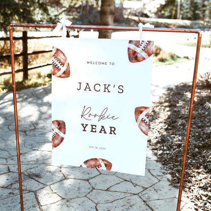 Rookie of the Year football first birthday welcome sign featuring vintage watercolor brown footballs, personalized birthday lettering, and a white background, displayed outdoors on a wooden easel.