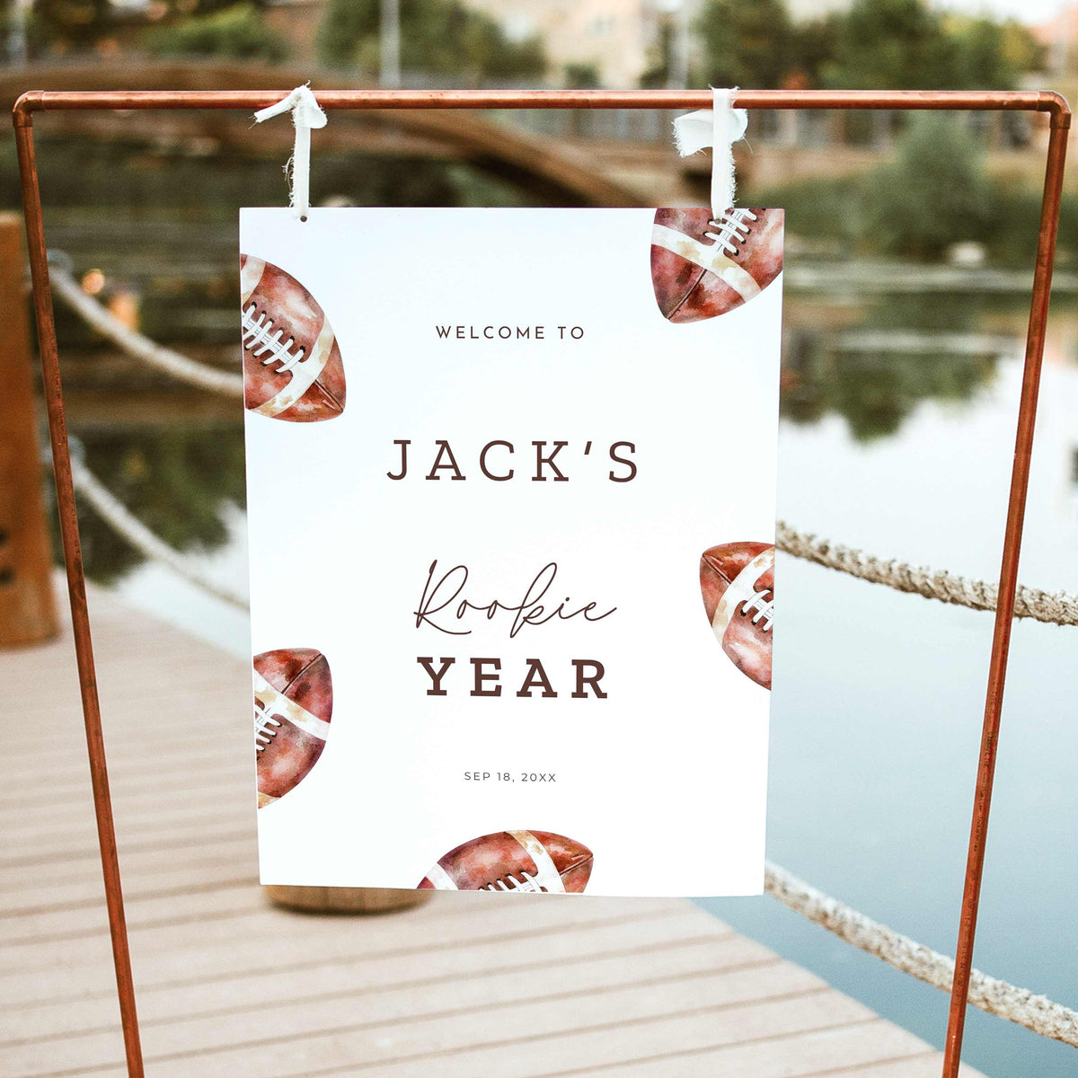 Rookie of the Year football first birthday welcome sign featuring vintage watercolor brown footballs, personalized birthday lettering, and a white background, displayed outdoors on a wooden easel.