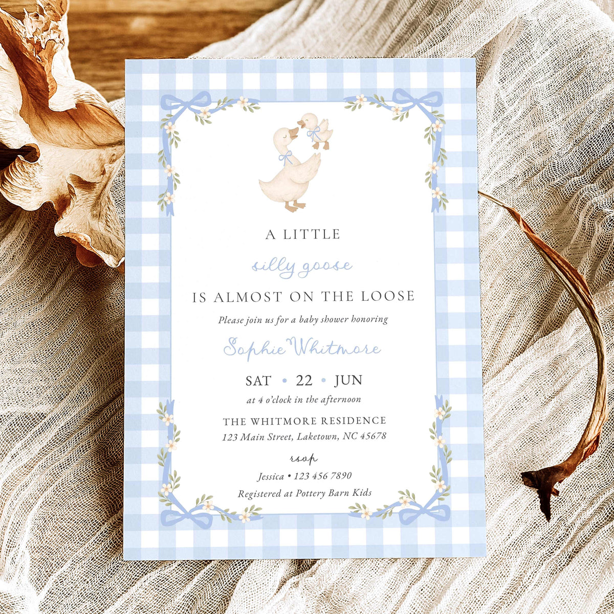 A baby shower invitation card featuring a light blue and white gingham border, a central white panel with a cute duckling illustration, and blue floral accents.
